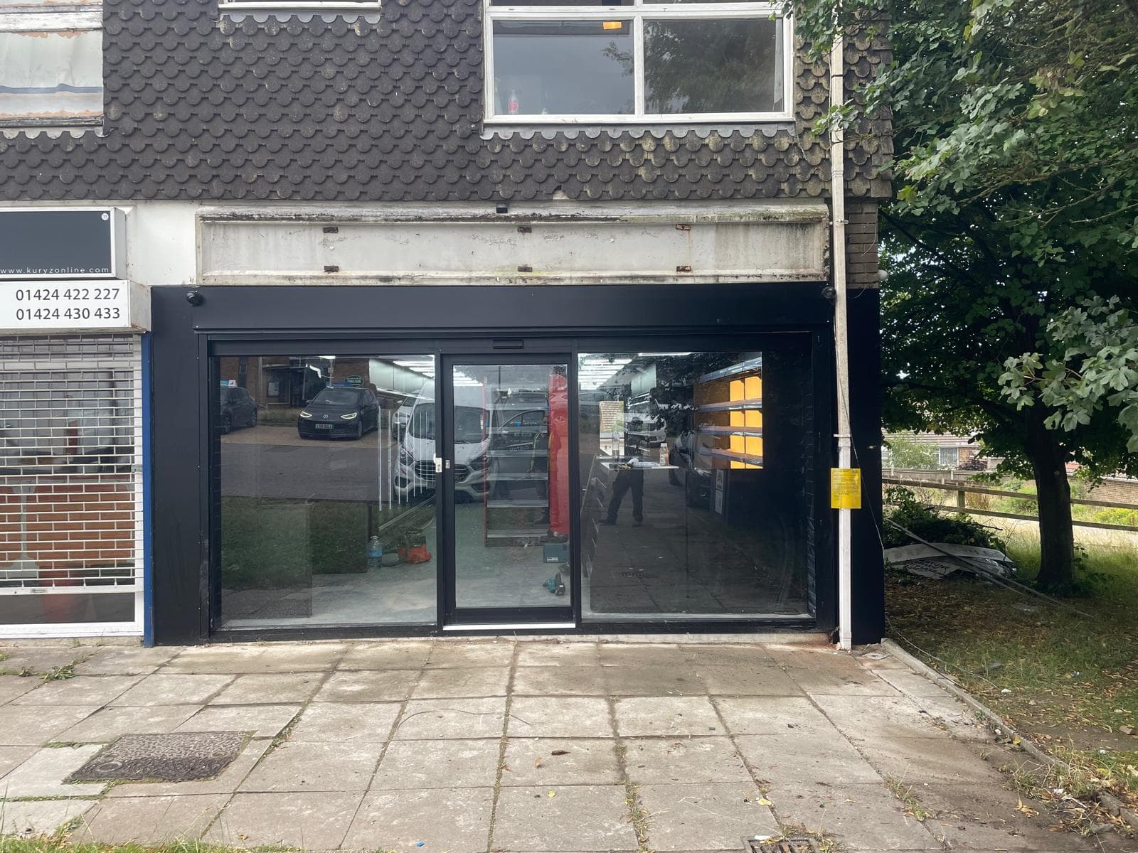 Single-storey shop with a new dark aluminium glazed front and sliding doors, a roller shutter on the neighbouring unit