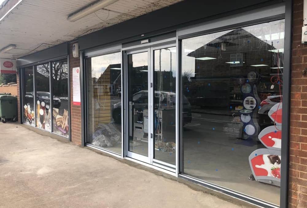 Shop unit in a brick parade: dark aluminium front with sliding glazed entrance doors between fixed display panes.